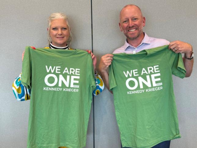 Two Kennedy Krieger staff members smile while holding green We Are One Kennedy Krieger t-shirts.