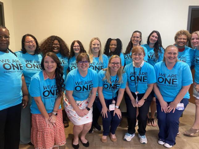 A large group photo of Kennedy Krieger staff members smiling while wearing blue We Are One t-shirts.