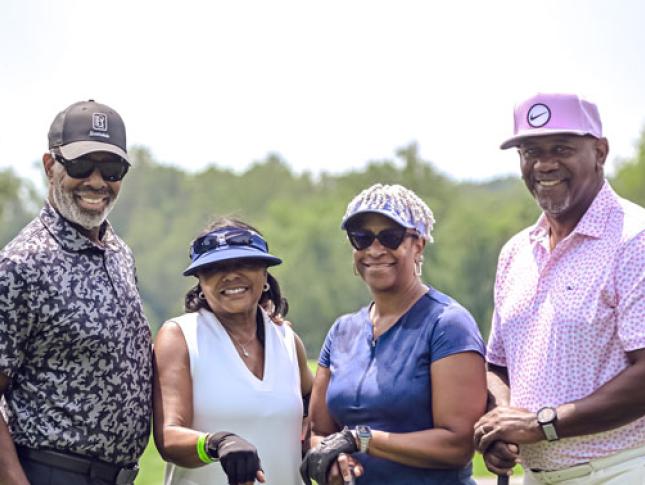 Two men and two women smile while standing at a golf course.