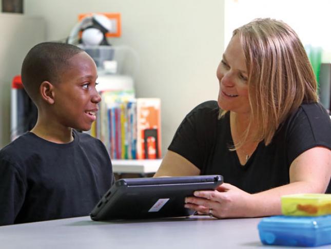 A teacher shows her student, a boy, content on a tablet.