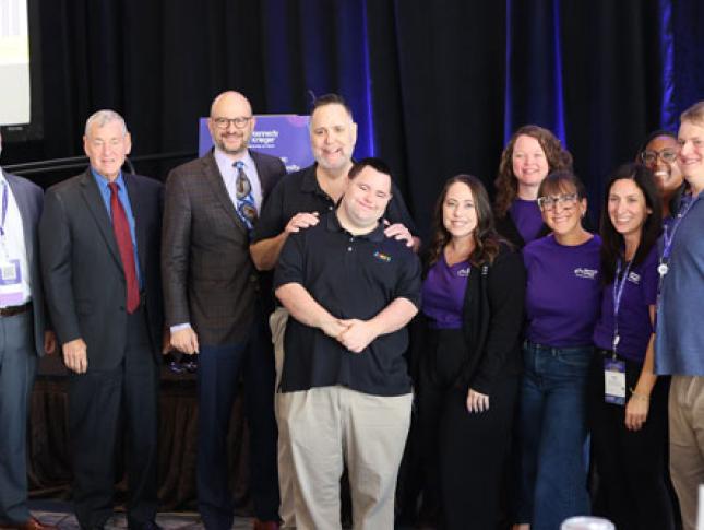 A group of Tapping into Talent Conference attendees smile while standing in front of a stage.