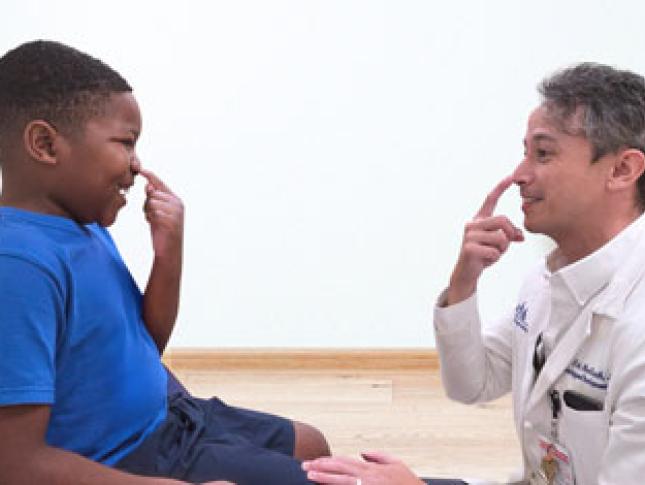 A young boy and his doctor at Kennedy Krieger smile as they both touch their noses.