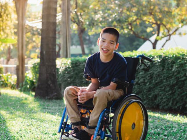 A boy in a wheelchair smiles while sitting outside.