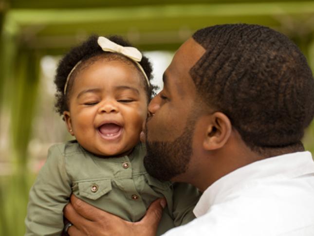 A father kisses his baby girl while holding her.