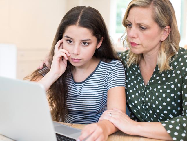 A mother comforts her daughter while they look at a laptop.