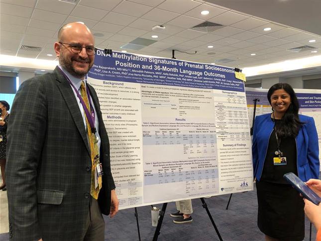 A man and a woman stand on opposite sides of a research poster. Both are smiling.