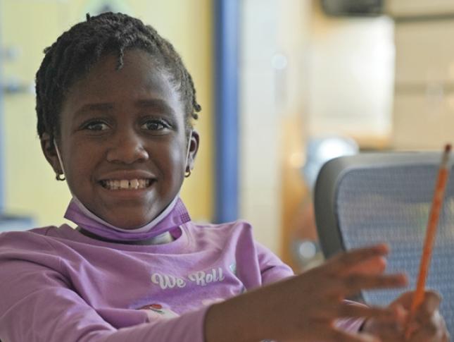 A Fairmount student sits at her desk holding a pencil.
