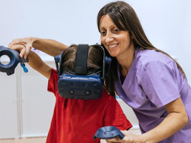 A boy is assisted by a therapist while using a virtual reality headset.