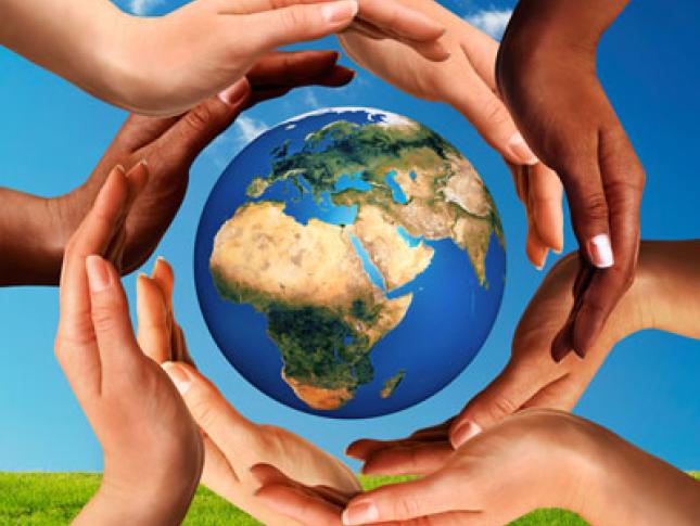 Hands making a circle together around the world the Earth globe on blue sky and green grass background.