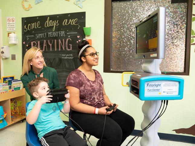 A WIN volunteer assists two kids as they play with a Starlight fun center game.