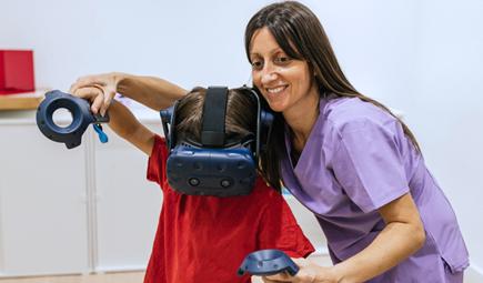 A boy is assisted by a therapist while using a virtual reality headset.