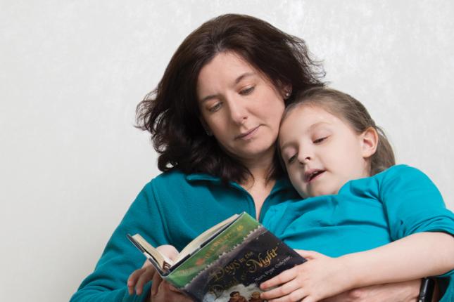 Caetlyn lays in her mom, Caryn's lap, as Caryn reads a book to her.