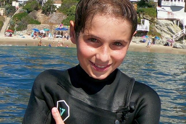 A photo of Brayden in a wetsuit, posing in front of an ocean