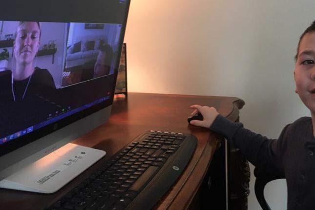 A photo of a Kennedy Krieger student sitting in front of a computer during a virtual school lesson