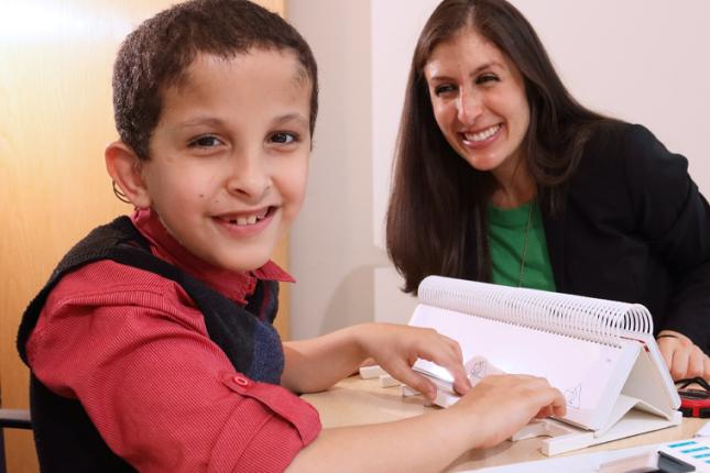 A young patient types on his speech device as he sits with his therapist