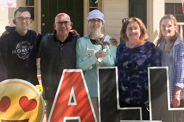 Ally stands with her family behind red and black letters spelling out her name.