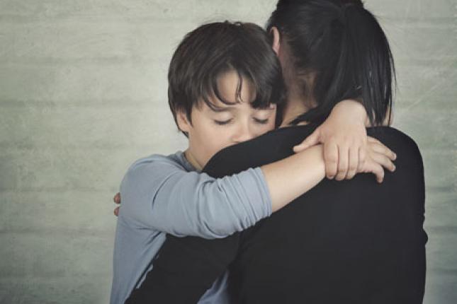 Sad child hugging his mother against a light brick background