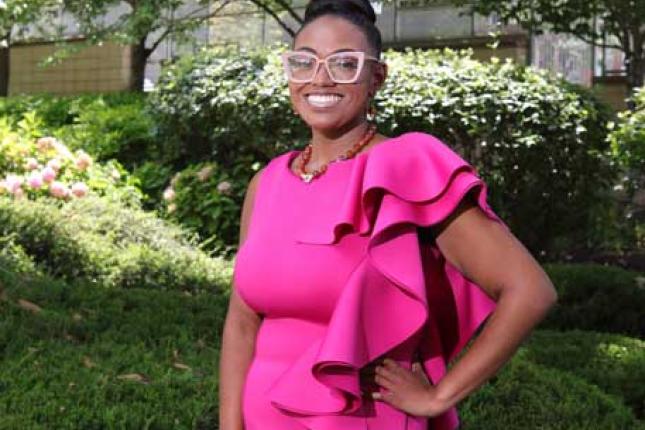 A young woman stands outside. She is smiling and appears confident.