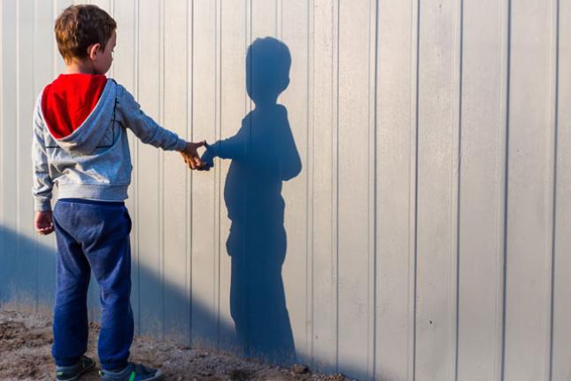A boy with autism looks at and touches his shadow casted on a wall. 