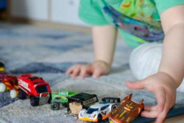 A child plays with small toy cars and trucks in a straight line.