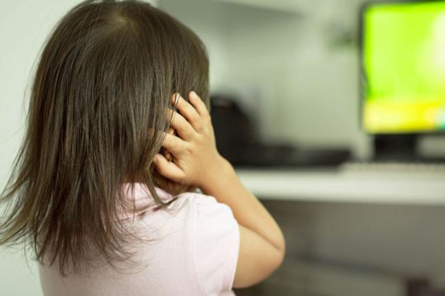 A child afraid of loud sounds covers its ears while standing in front of a tv.