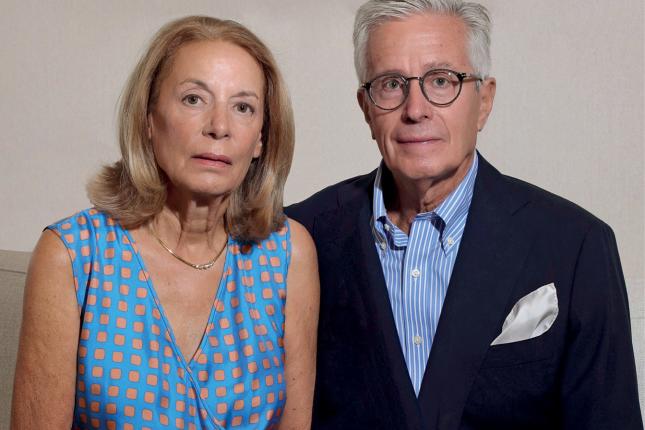 Portrait photo of a woman wearing a dress and necklace and a man wearing glasses and a suit with no tie