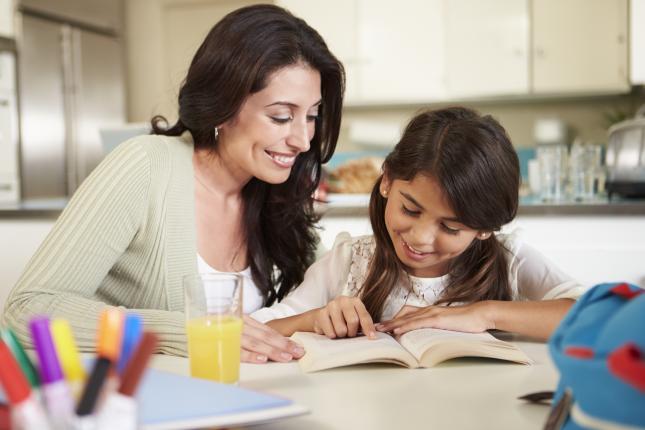 A woman and her daughter read together while sitting at the kitchen counter.