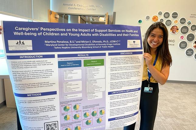 Martina Penalosa smiles as she stands next to her research poster, entitled "Caregivers’ Perspectives on the Impact of Support Services on Health and Well-being of Children and Young Adults with Disabilities and their Families