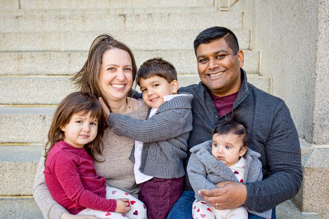 A family portrait of a mother and father, with a little boy and girl, and a baby girl. Everyone but the baby is smiling.