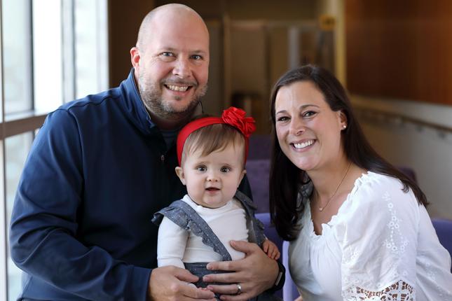 A baby girl sits with her parents.