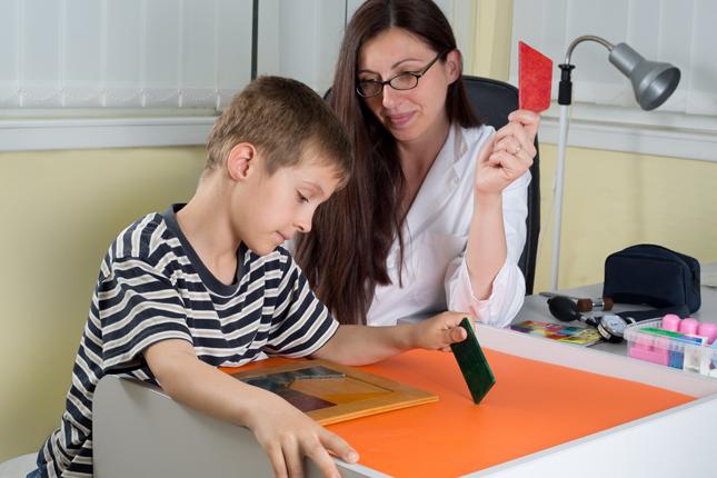 A child puts together a puzzle of shapes with help from an adult.