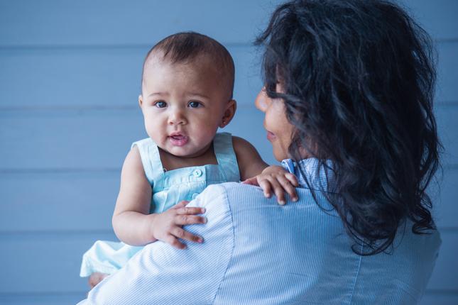 A little baby girl in her mom's arms, against a gray background