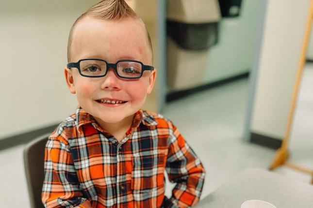 A young boy with Sturge-Weber syndrome, a rare disease, sits at a table and smiles. 