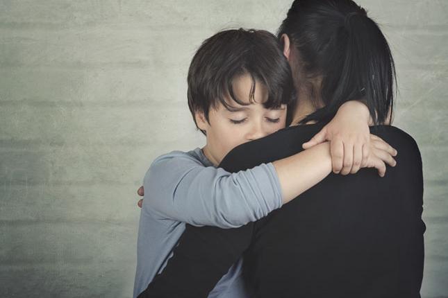 Sad child hugging his mother against a light brick background