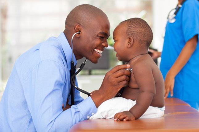 A male doctor smiles while examining a baby boy.