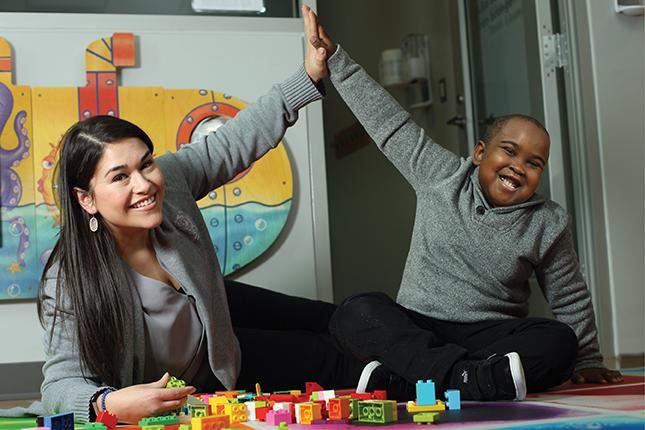 A teacher and a young boy high-five each other while playing with Lego bricks.