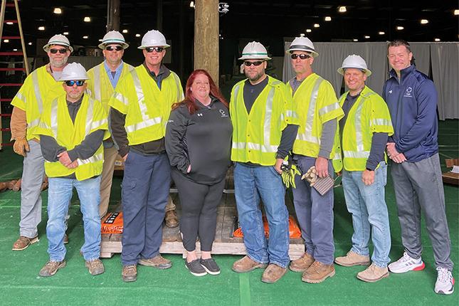 A group of nine people, mostly men and mostly wearing bright yellow construction vests and helmets, pose for the camera.