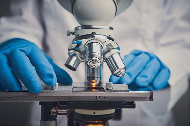 Two latex-gloved hands operate a microscope.