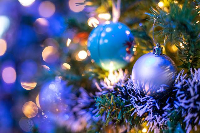 Closeup of Christmas ornaments hanging on a brightly lit tree.