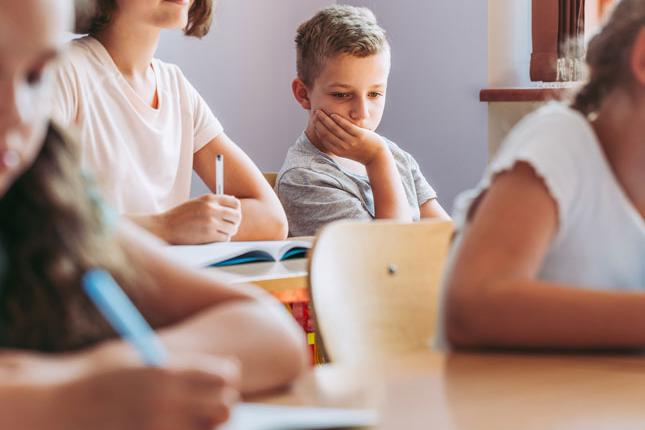 A sad boy sitting in the back of the classroom during school.