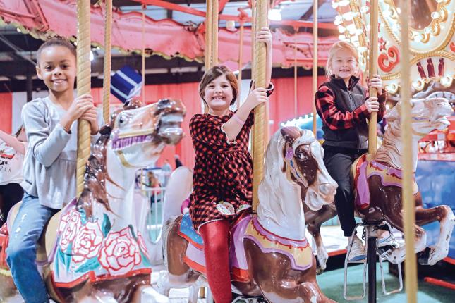 Three little girls smile while riding a carousel at Kennedy Krieger's annual Festival of Trees.
