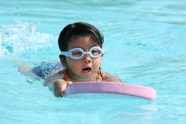 A boy swims in a swimming pool while using a paddle board.