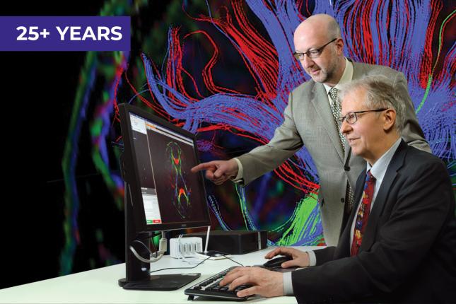 Two men in business suits work at a computer, which displays a colorful MRI image of a human brain.