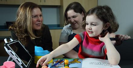 Dr. Landa sits with a patient and her mother as she reads a book