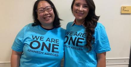 Two women smile while wearing t-shirts that say We Are One Kennedy Krieger.