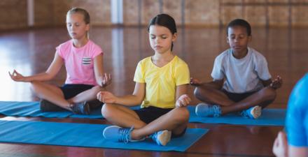 Three children sit on yoga mats while meditating.