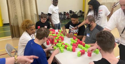 Neurodiversity at Work interns sit a table organizing green and read cylinders.