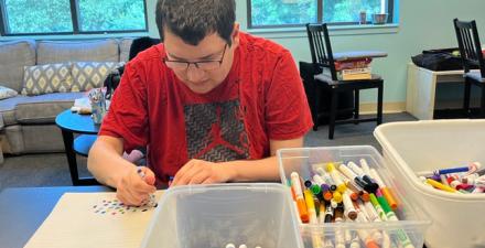 A Neurodiversity at Work intern sits at his desk writing. 