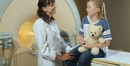 A doctor with a child sitting on an MRI machine.