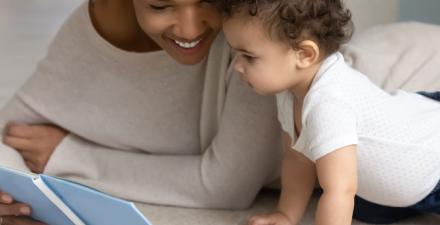 A mother and her small child smile while looking at a book.